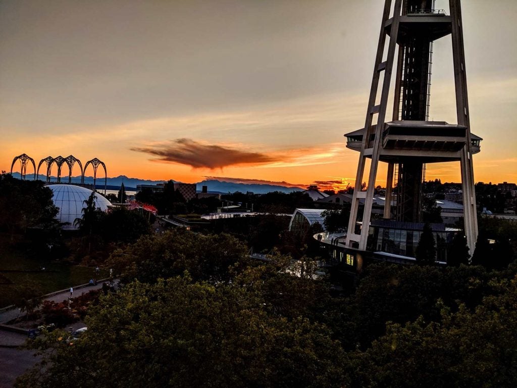 View of the sunset in the distance.  Also visible is the lower half of the Space needle, the arches of the Pacific Science Center, a dome, and lots of trees. 