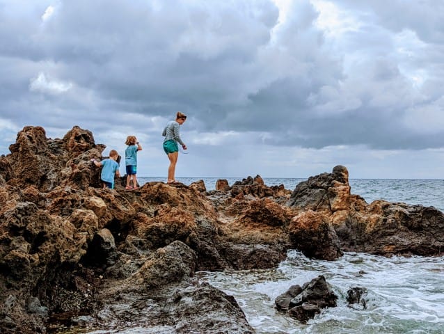 A mother and two children climb sharp rocks near the ocean