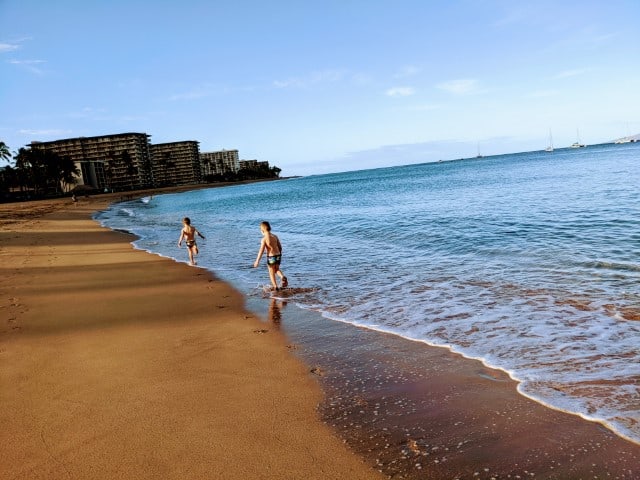 Two children, wearing swimsuits, run down Maui's Kaanapali beach splashing in the surf